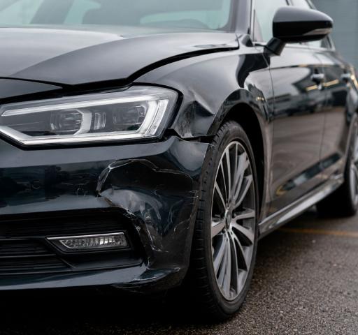 Wgniecione drzwi ciemnego samochodu po szkodzie parkingowej